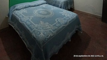 Una habitación con dos camas, un ventilador de techo, una lámpara fijada a la pared y un cuadro enmarcado.