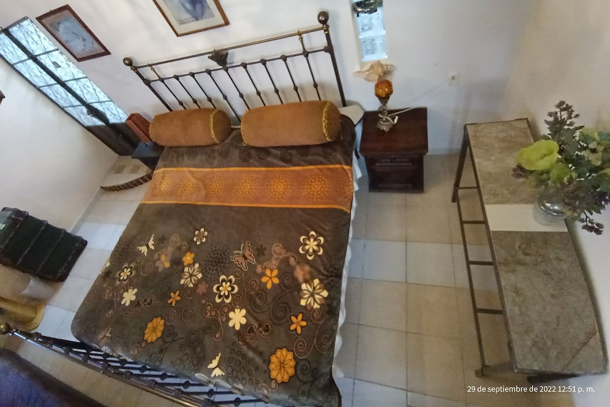 Un dormitorio con cama, mesitas de noche, una pequeña mesa y un jarrón con flores.