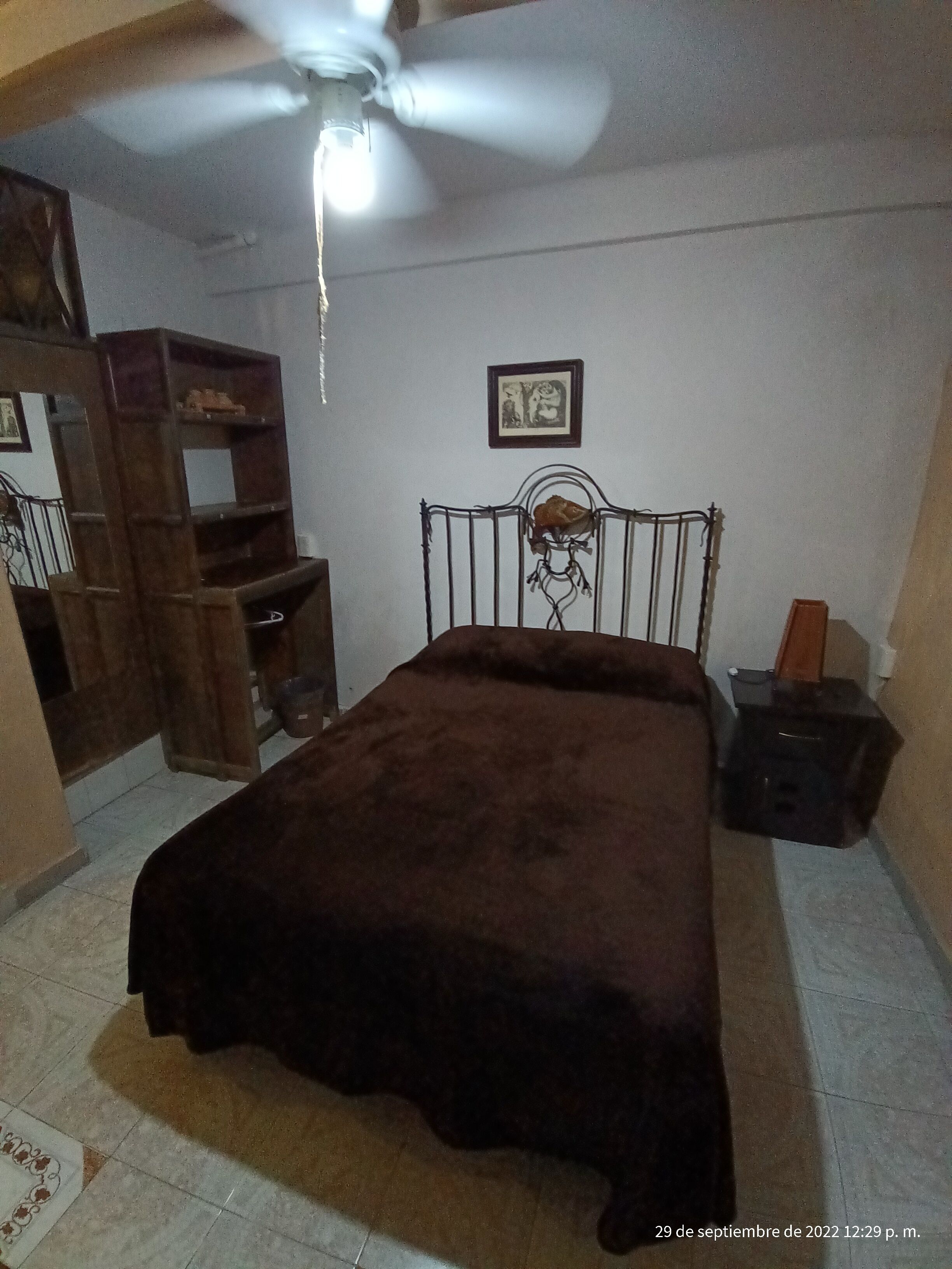 A bedroom with a bed, a ceiling fan, a wooden shelf, and a framed picture on the wall.
