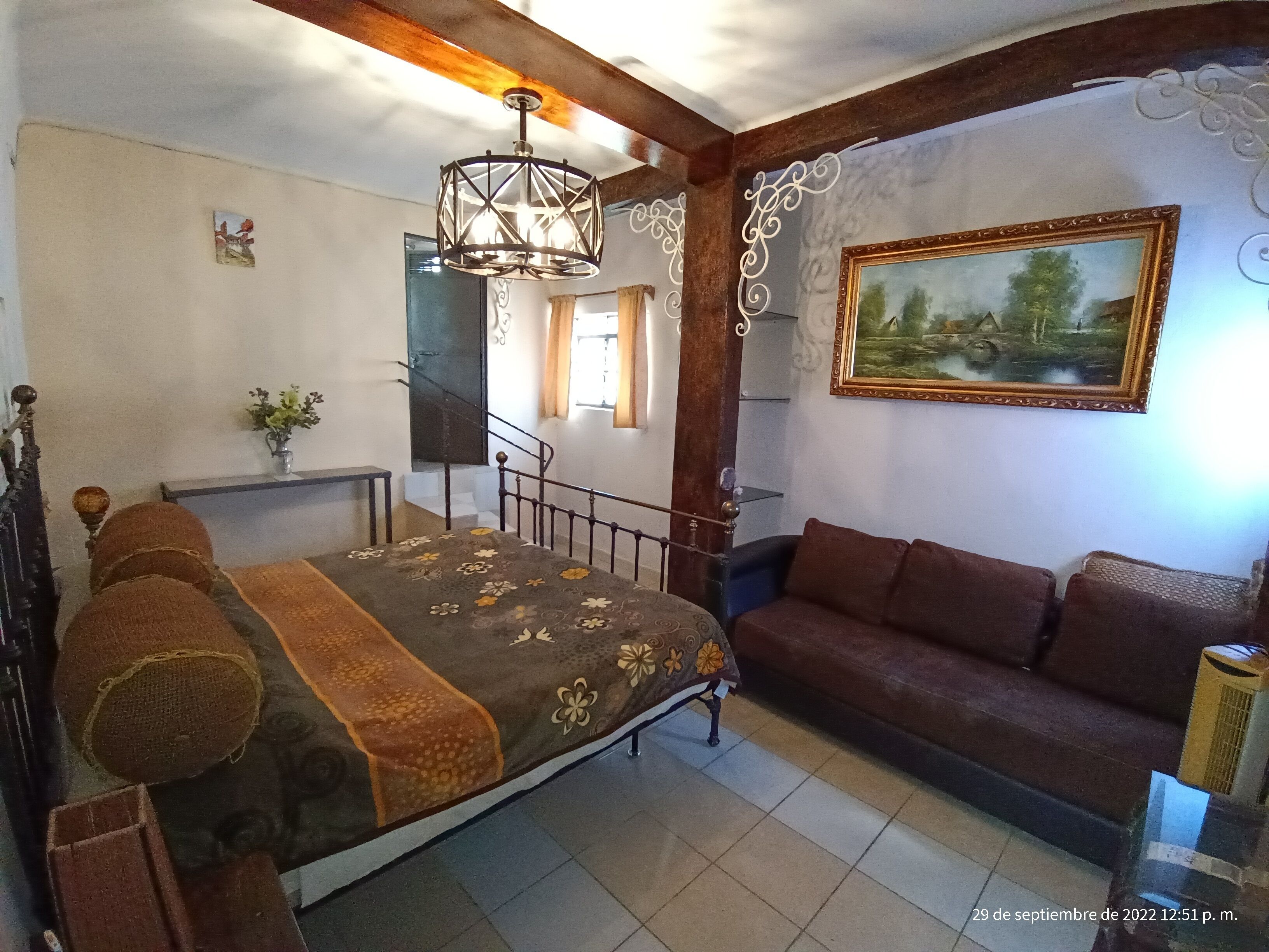 A bedroom with a bed, a sofa, a staircase, and a painting on the wall.
