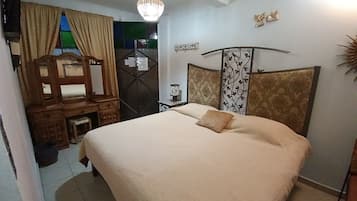 Un dormitorio con una cama grande, un escritorio de madera, un espejo, una araña y detalles decorativos en la pared.