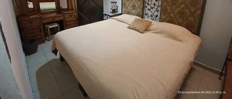 Un dormitorio con una cama grande, un escritorio de madera, un espejo, una araña y detalles decorativos en la pared.