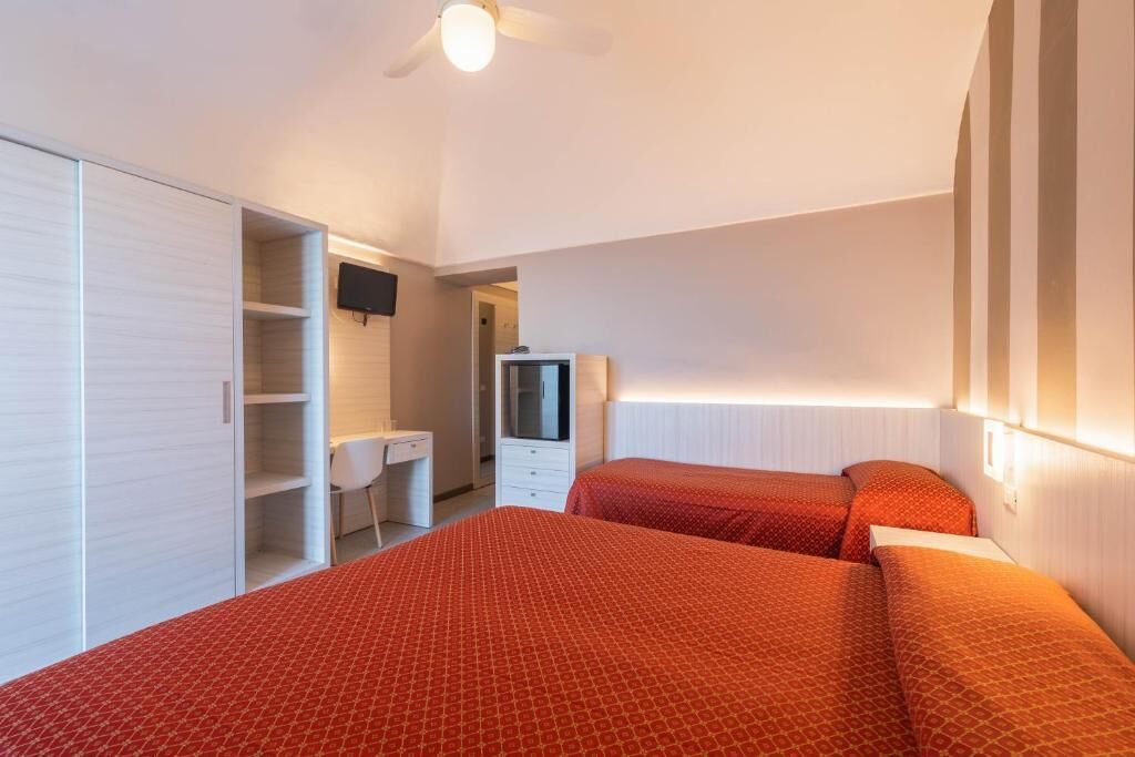 Quarto com duas camas, uma escrivaninha, um guarda-roupa e uma televisão.
