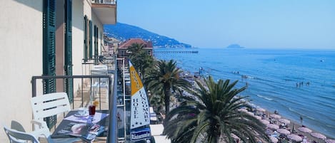 A balcony with a view of a beach, palm trees, and a pier in the distance.