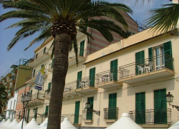 A multi-story building with balconies, green shutters, and a palm tree in front. - Hotel Danio Lungomare (Alassio)