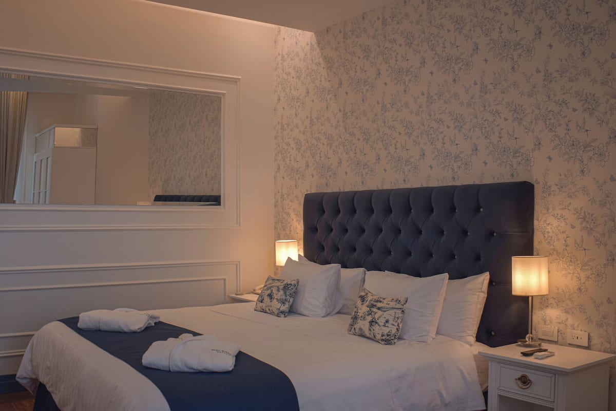 A neatly made bed with a tufted headboard, two bedside lamps, and a mirror above the bed.