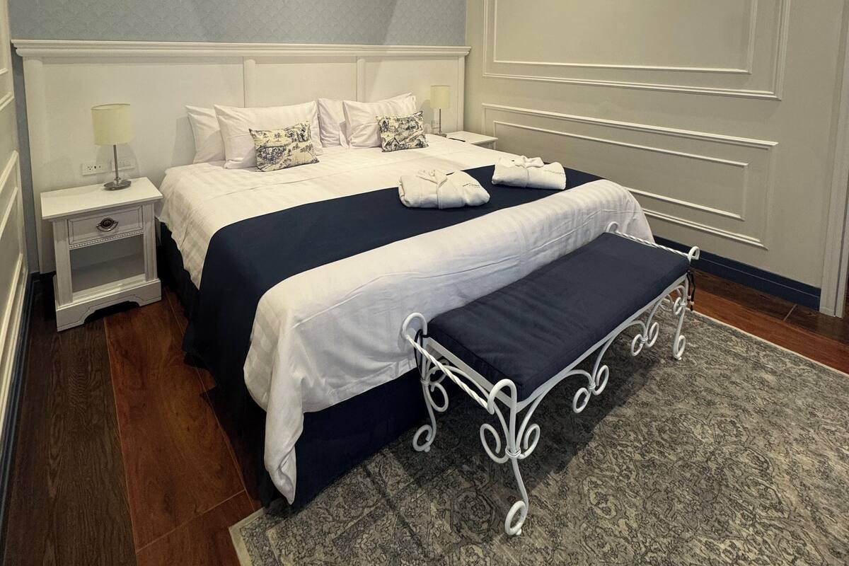 A modern hotel room with a large bed, bedside tables, and a patterned rug.