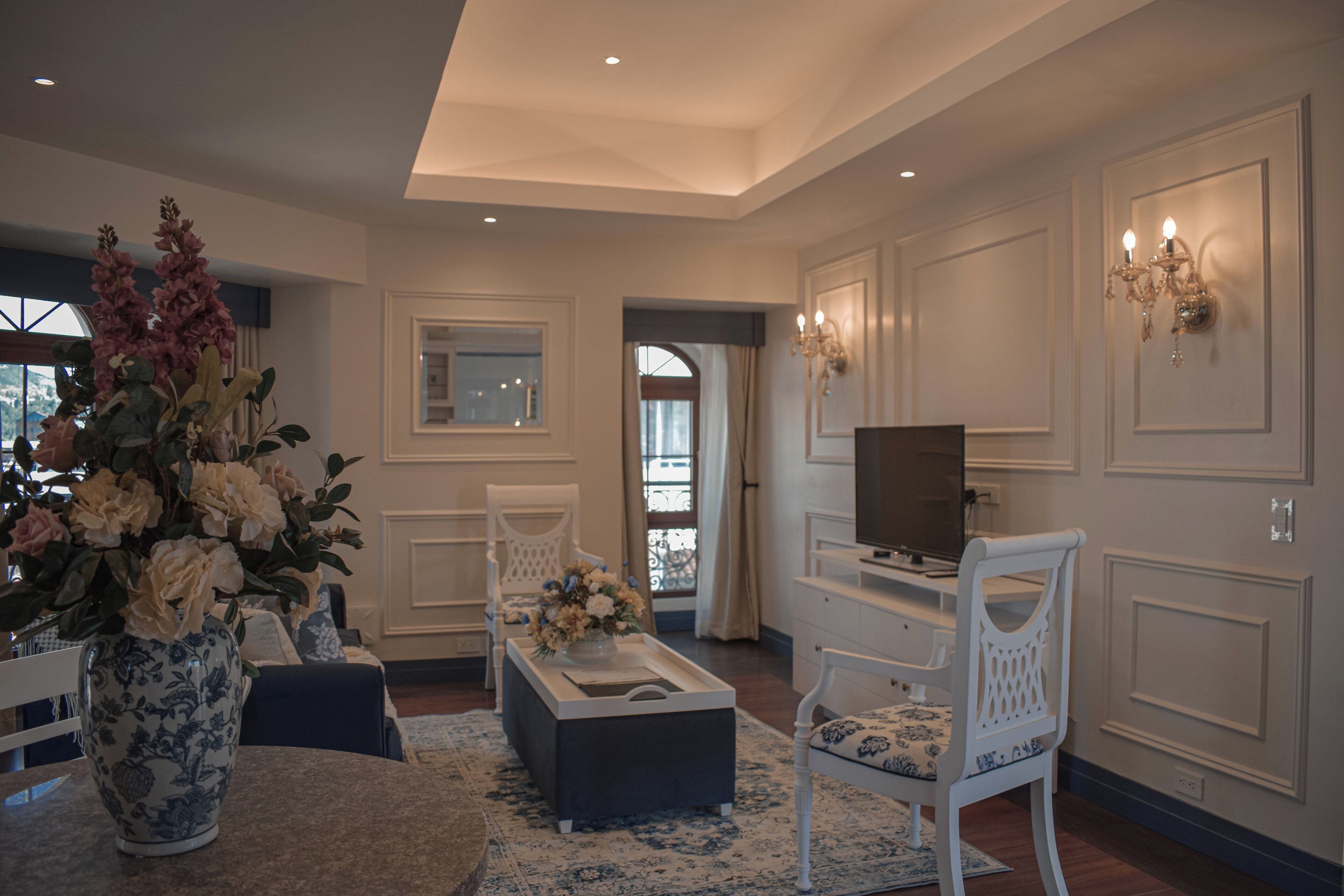 A spacious living room with a large vase of flowers, a television, and a dining area with a table and chairs.