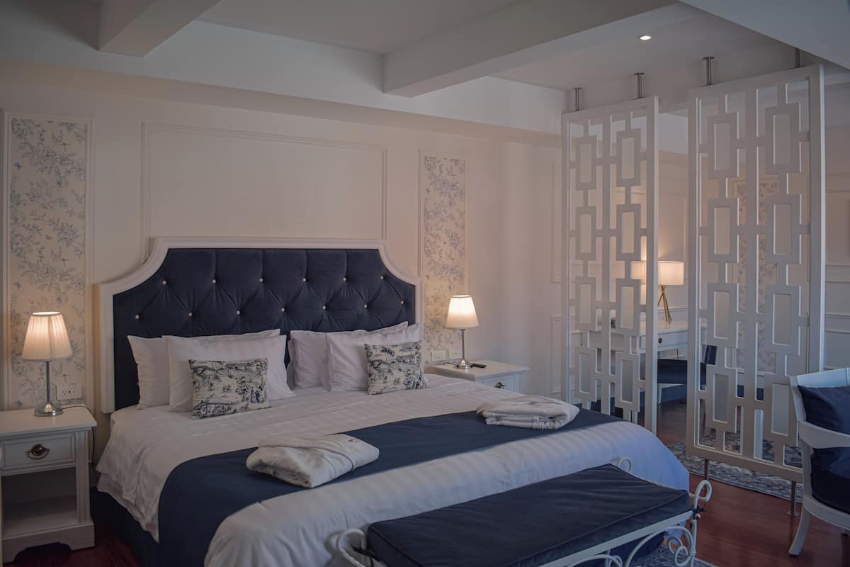 A hotel room with a large bed, two bedside tables, a nightstand, a chair, and a decorative screen.