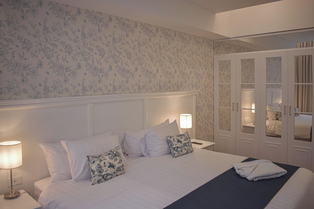 A hotel room with a bed, nightstands, a wardrobe, and a mirror.