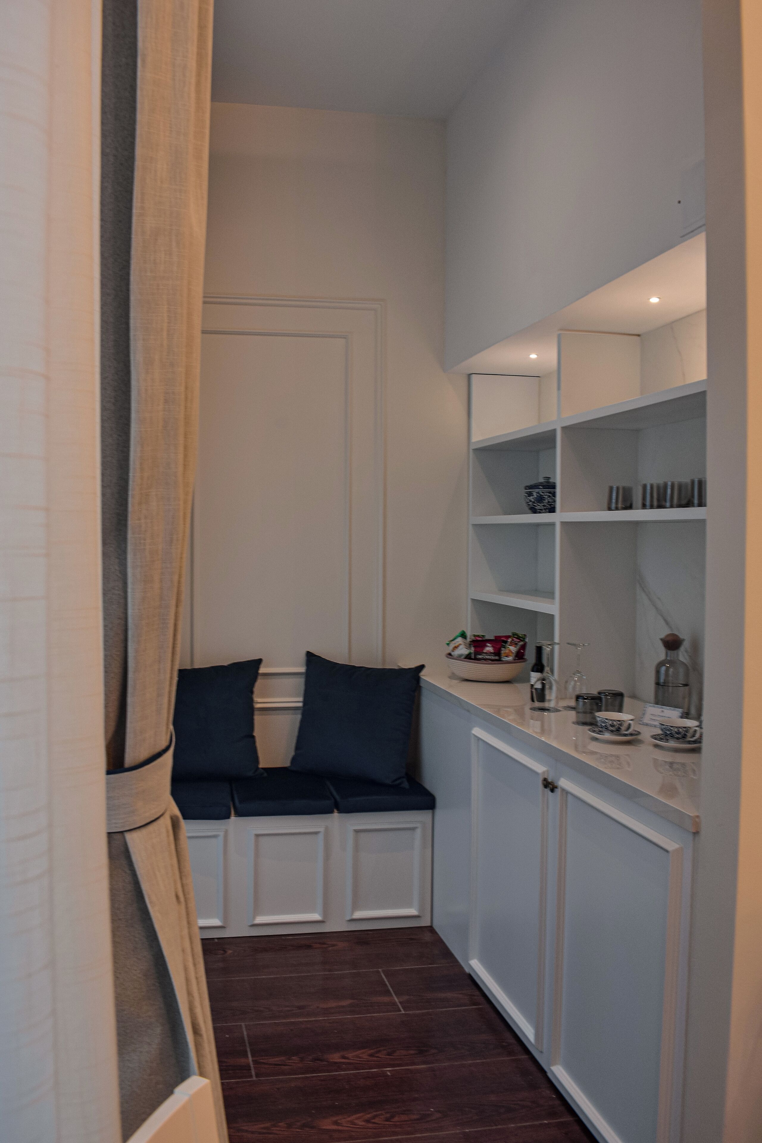 A narrow hallway with a bench, a mirror, and shelves with toiletries.