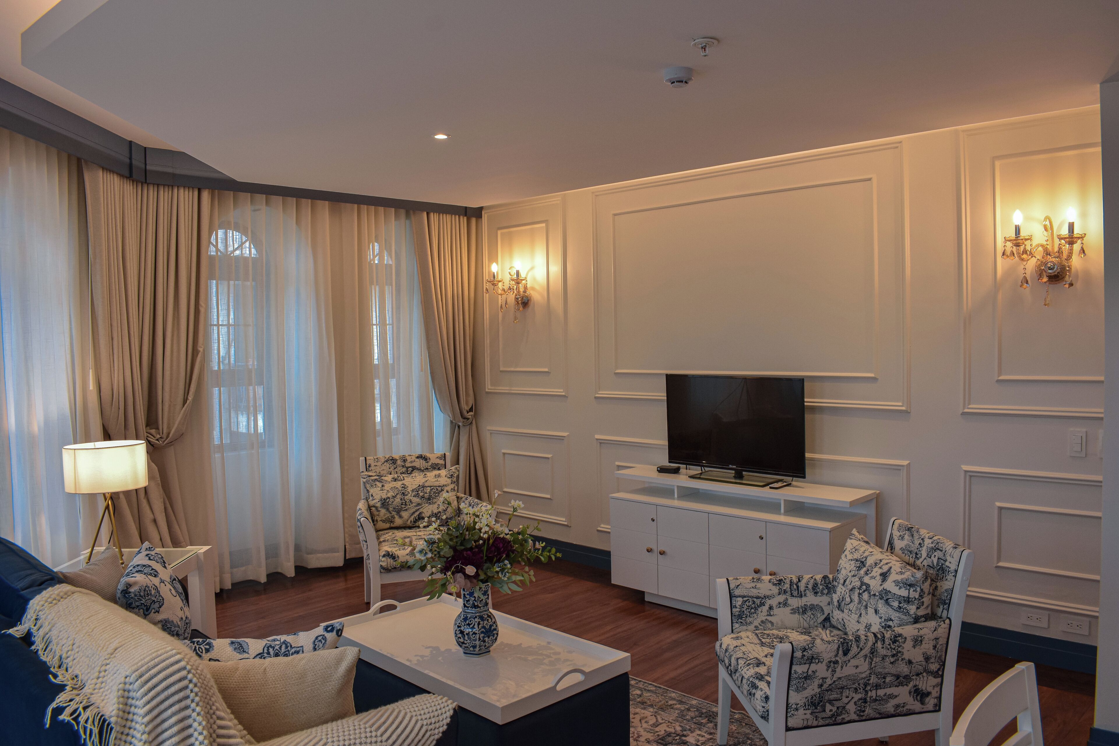 A living room with a sofa, armchairs, a coffee table with a vase, a TV on a cabinet, and a lamp.