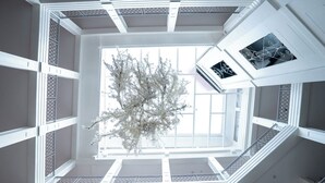 A high-ceiling atrium with a central tree, large windows, and a staircase. - Parc Royale Suites Hotel (Cuenca)