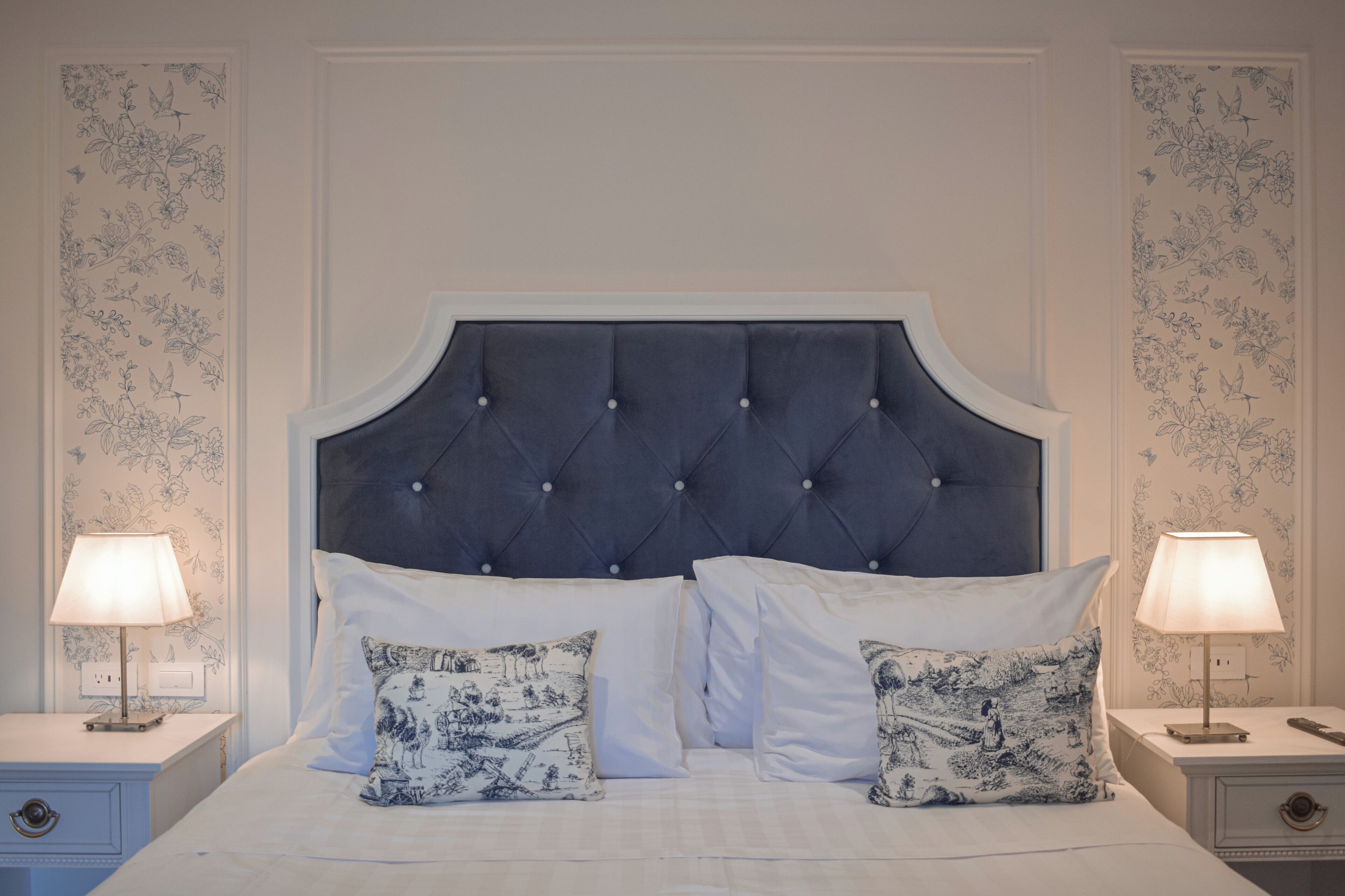 Une chambre à coucher avec une tête de lit capitonnée, du linge de lit blanc et deux lampes de chevet.