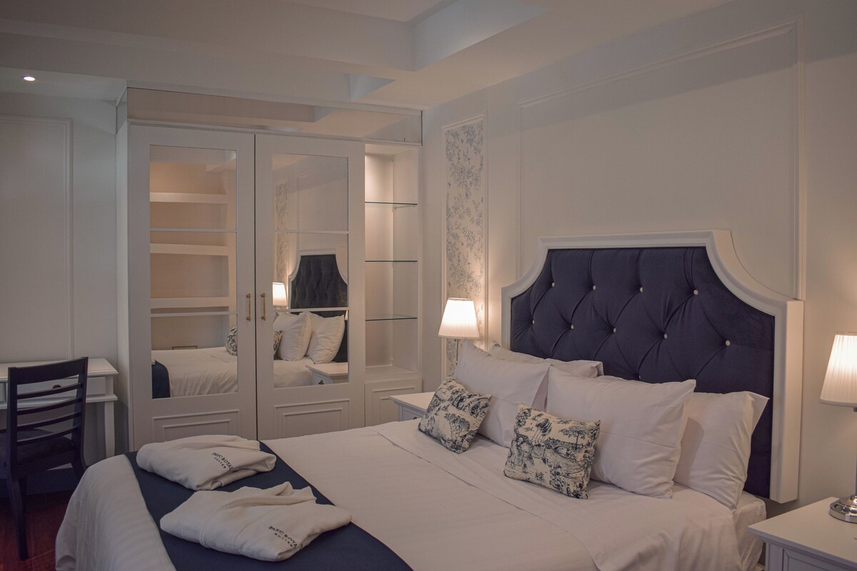A bedroom with a large bed, a wardrobe with glass doors, and a desk.