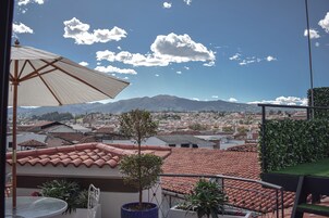 Un balcón con vistas a la ciudad, un árbol en maceta y un paraguas grande.