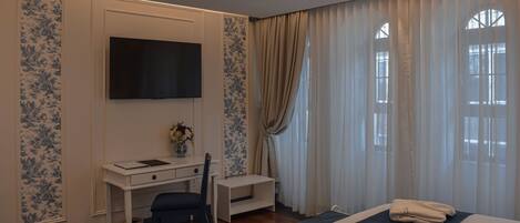A hotel room with a bed, a desk, a chair, a TV, and a window with curtains.