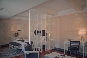 Un dormitorio con cama, escritorio, silla, lámpara y un biombo decorativo.