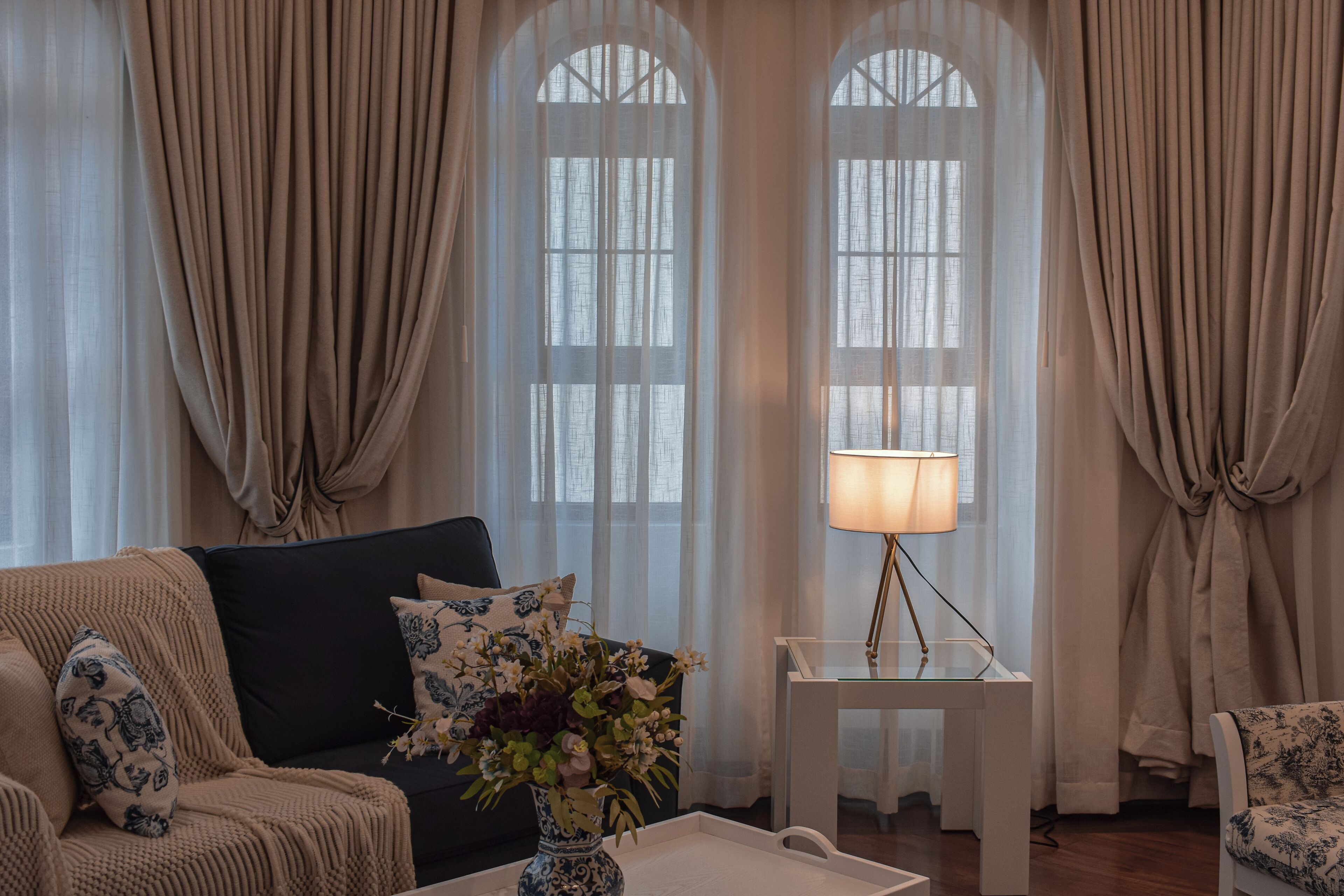A living room with a sofa, a small table with a lamp, and a vase with flowers.