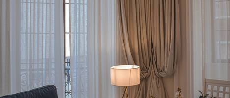 Una sala de estar con un sofá azul oscuro, una mesita auxiliar blanca, una lámpara y un jarrón con flores.