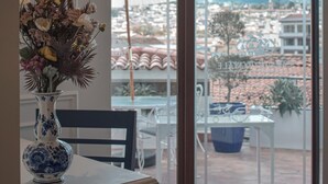 A balcony with a table and chairs, a vase with flowers, and a view of a cityscape through large windows. - Parc Royale Suites Hotel (Cuenca)