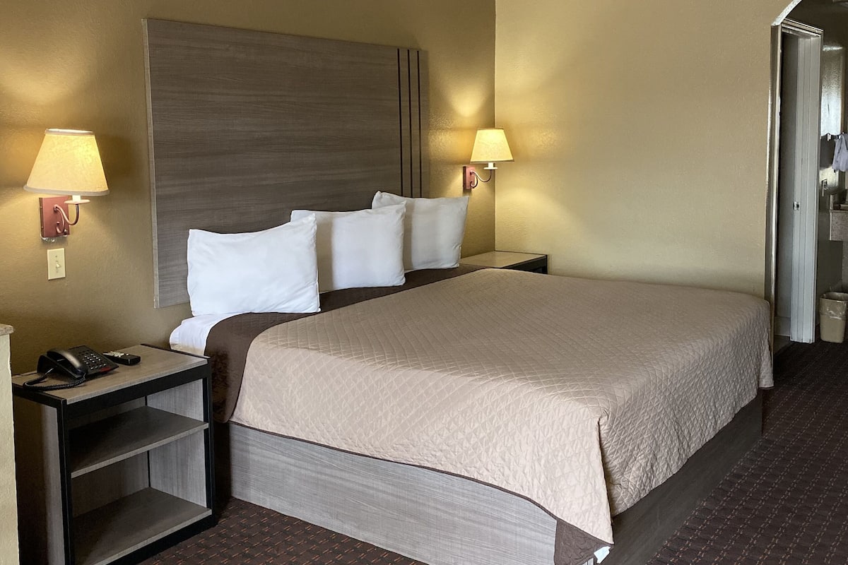 Quarto de hotel com uma cama grande, duas mesas de cabeceira, um telefone e duas luminárias de parede.
