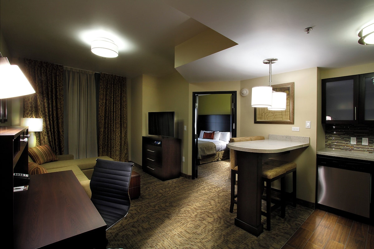 Een hotelkamer met een eethoek, een bed met hoofdeinde, een televisie en een kitchenette.