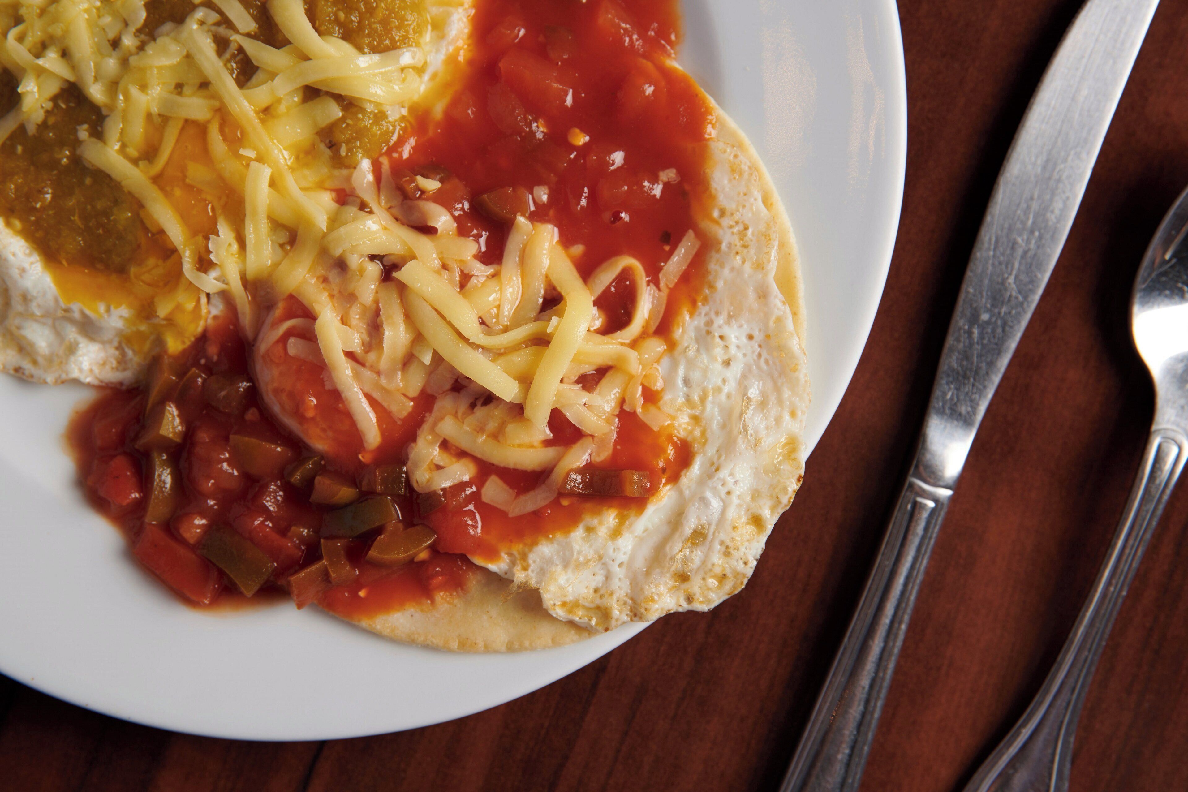 A plate with a sandwich, tomato sauce, and shredded cheese.