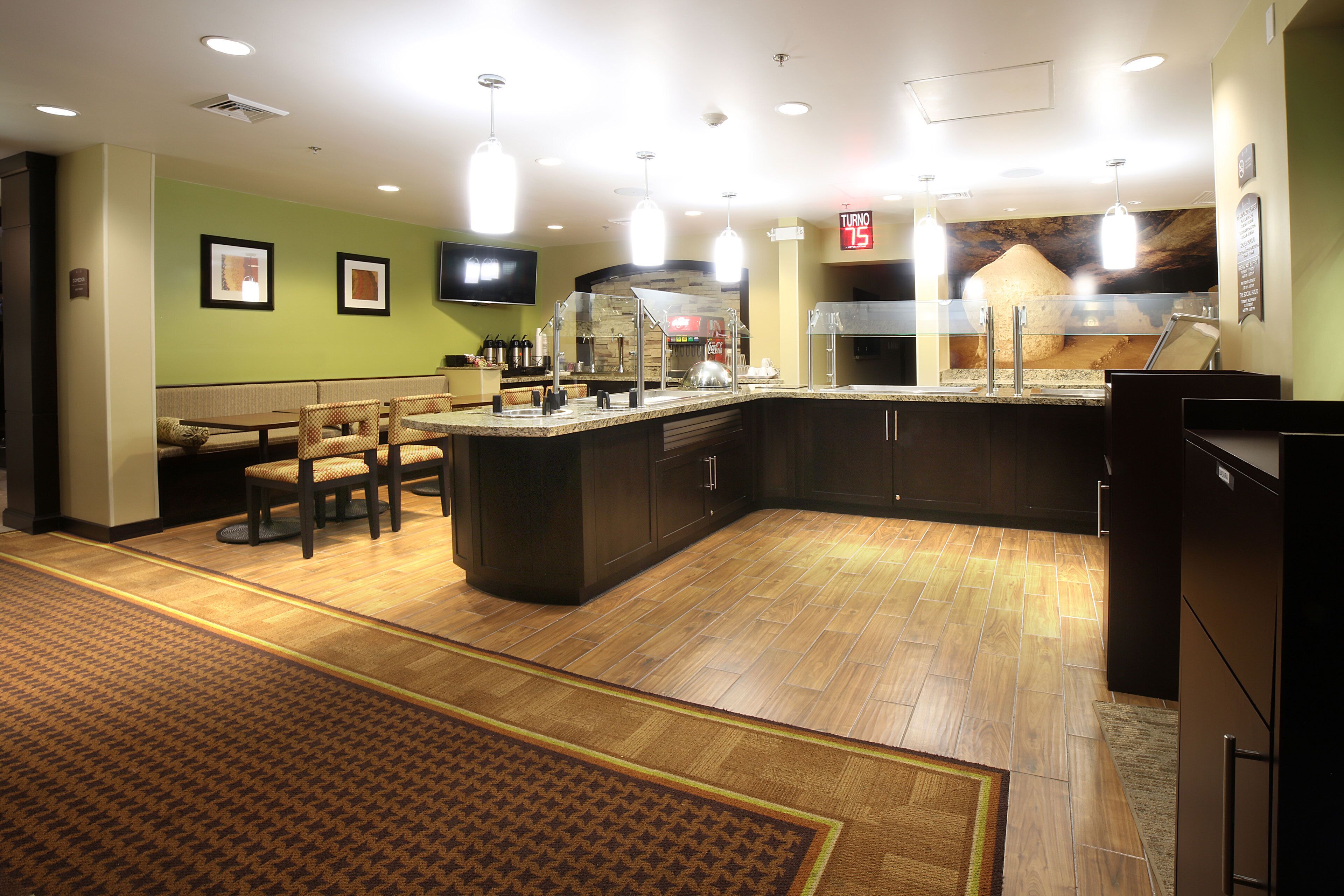 A hotel lobby with a seating area, a counter with a glass enclosure, and a digital clock displaying the time.