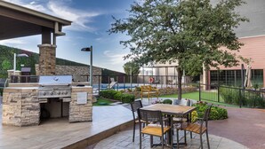 Une terrasse extérieure avec un barbecue en pierre, une table avec des chaises et une vue sur une piscine.