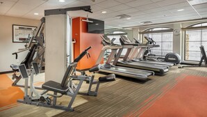 Une salle de sport équipée de tapis de course, d’appareils de musculation et d’un grand miroir.