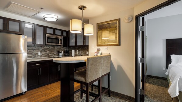 Una cocina moderna con armarios oscuros, electrodomésticos de acero inoxidable y una isla central con una silla.