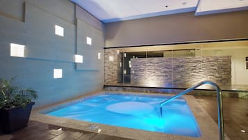 A hot tub with a stone wall backdrop and a wooden floor.