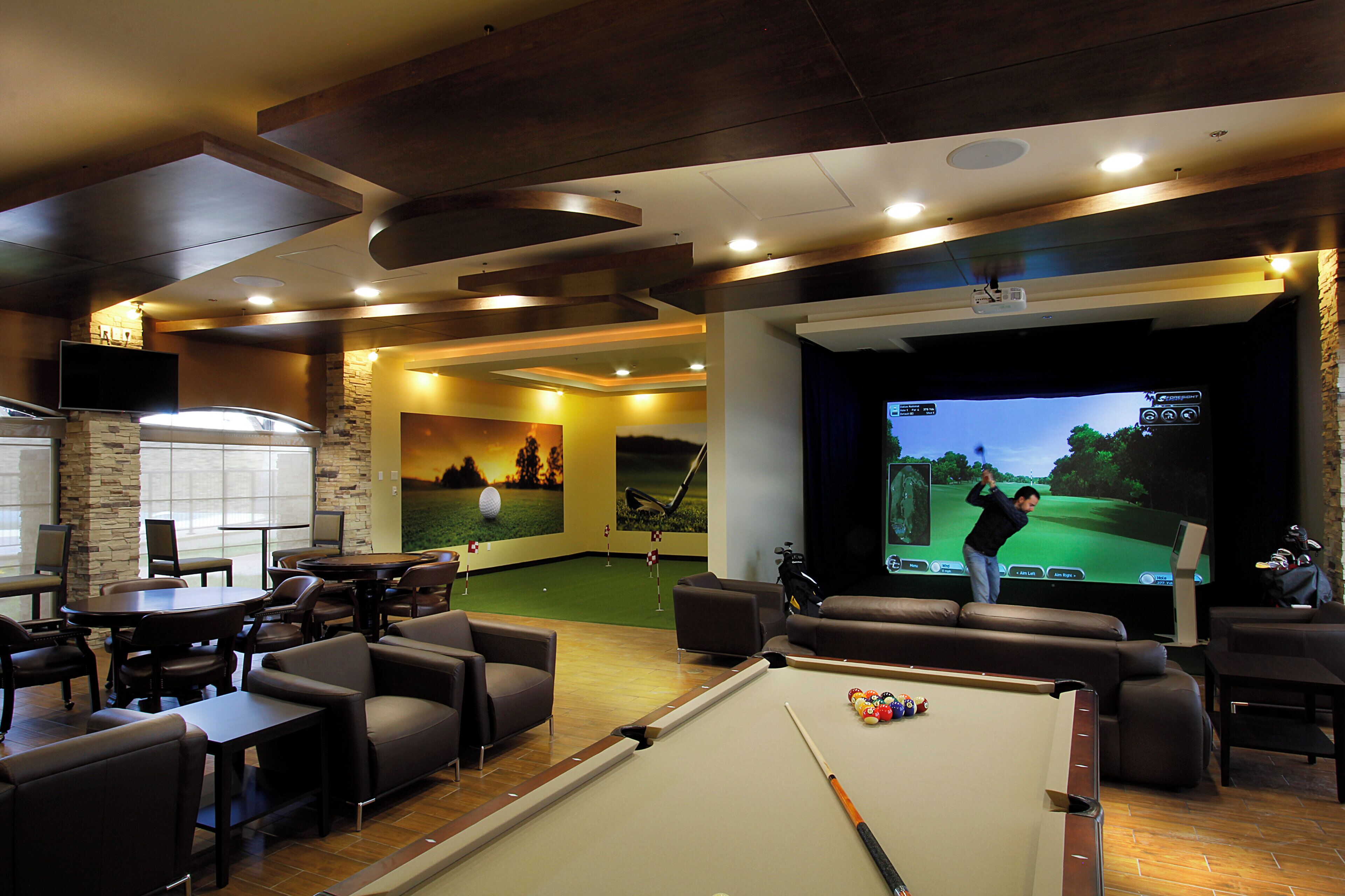 Una mesa de billar, asientos cómodos, una pantalla de proyección y un mural con temática de golf en un área de lounge.