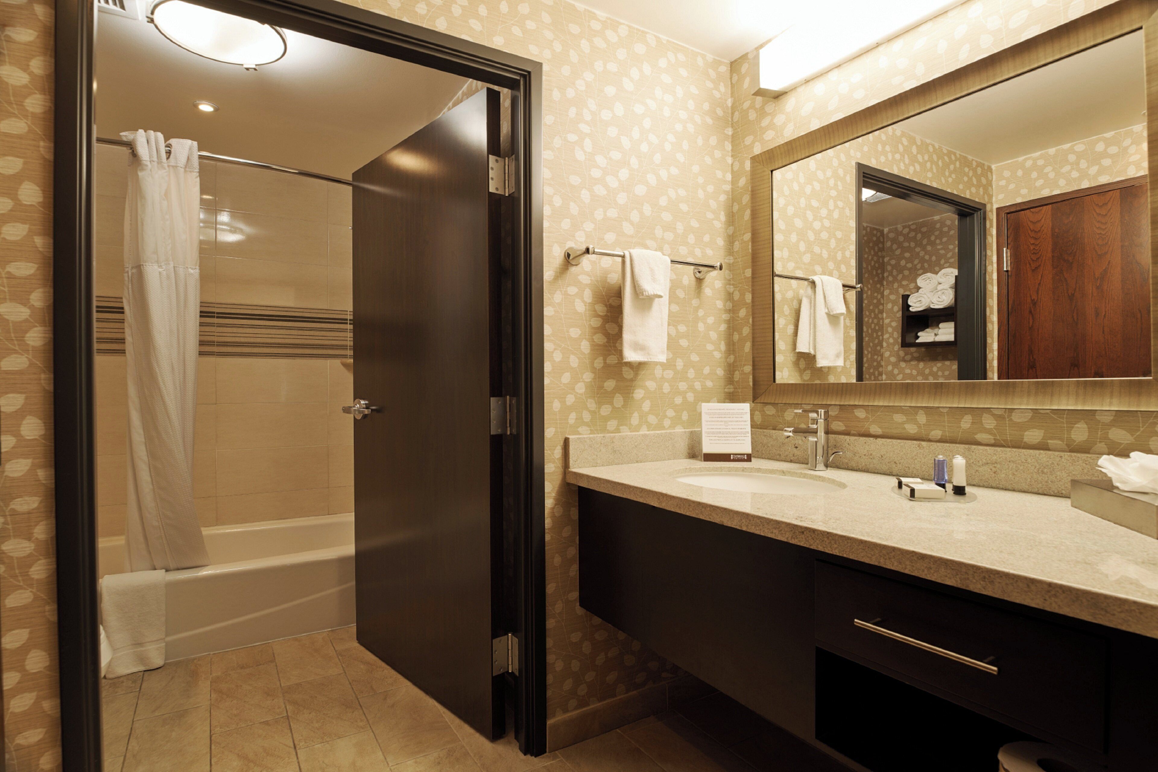 A bathroom with a shower, a sink, a mirror, and towels.