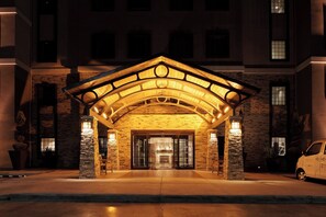A hotel entrance with a stone facade, a covered patio area, and a vehicle parked in front. - Staybridge Suites Chihuahua by IHG (Chihuahua)