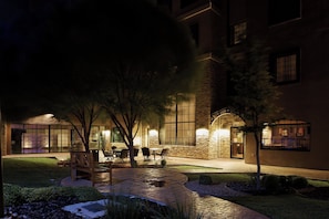 A building with a stone facade, large windows, and outdoor seating area with tables and chairs.