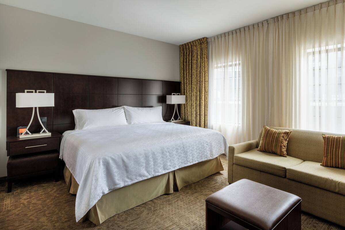 Een hotelkamer met een groot bed, een bank, een nachtkastje met lamp en een raam met gordijnen.
