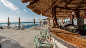 Un bar en la playa con techo de paja, sillas de descanso y vista al océano.