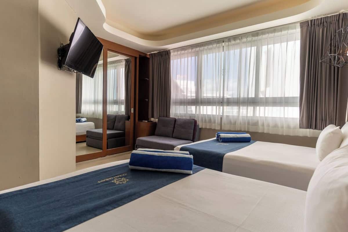 Ein Hotelzimmer mit zwei Betten, einem Sofa, einem Fernseher und großen Fenstern mit Vorhängen.