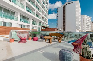 Terraza en la azotea con mobiliario exterior, piscina y vistas a edificios cercanos.