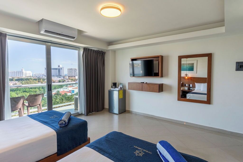 Habitación de hotel con dos camas, televisión, espejo y vistas de la ciudad.