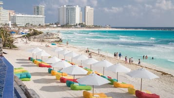 Na praia, areia branca, espreguiçadeiras, guarda-sóis