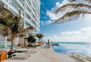 A resort pool area with lounge chairs, palm trees, and a view of the ocean. - Ocean Dream Cancun by GuruHotel (Cancun)