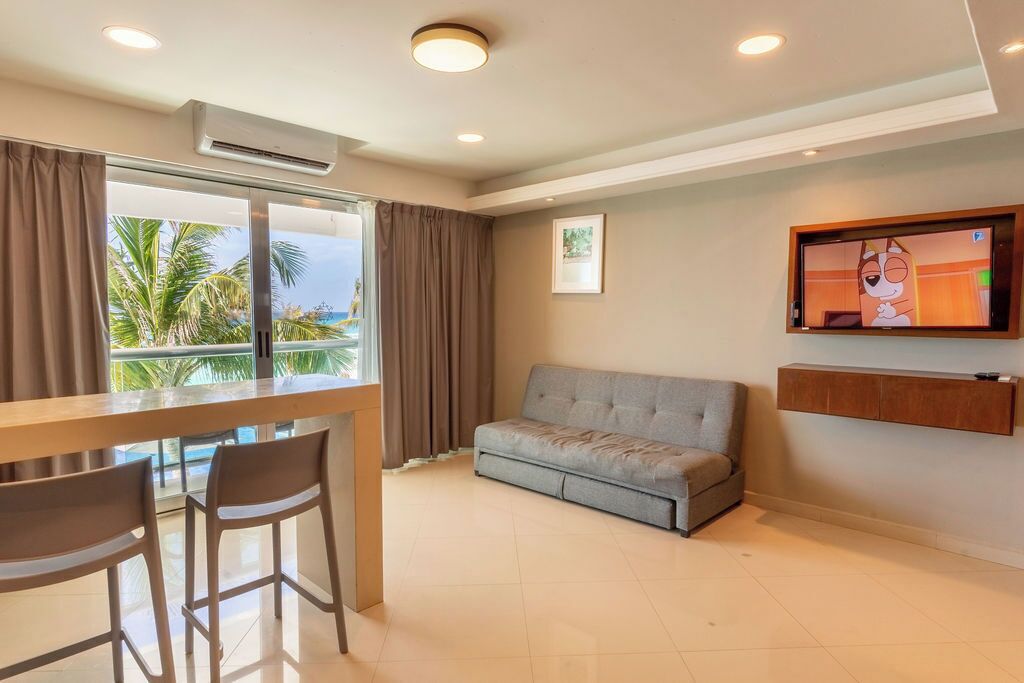Una sala de estar moderna con sofá, televisor, mesa de comedor con sillas y un ventanal con cortinas.