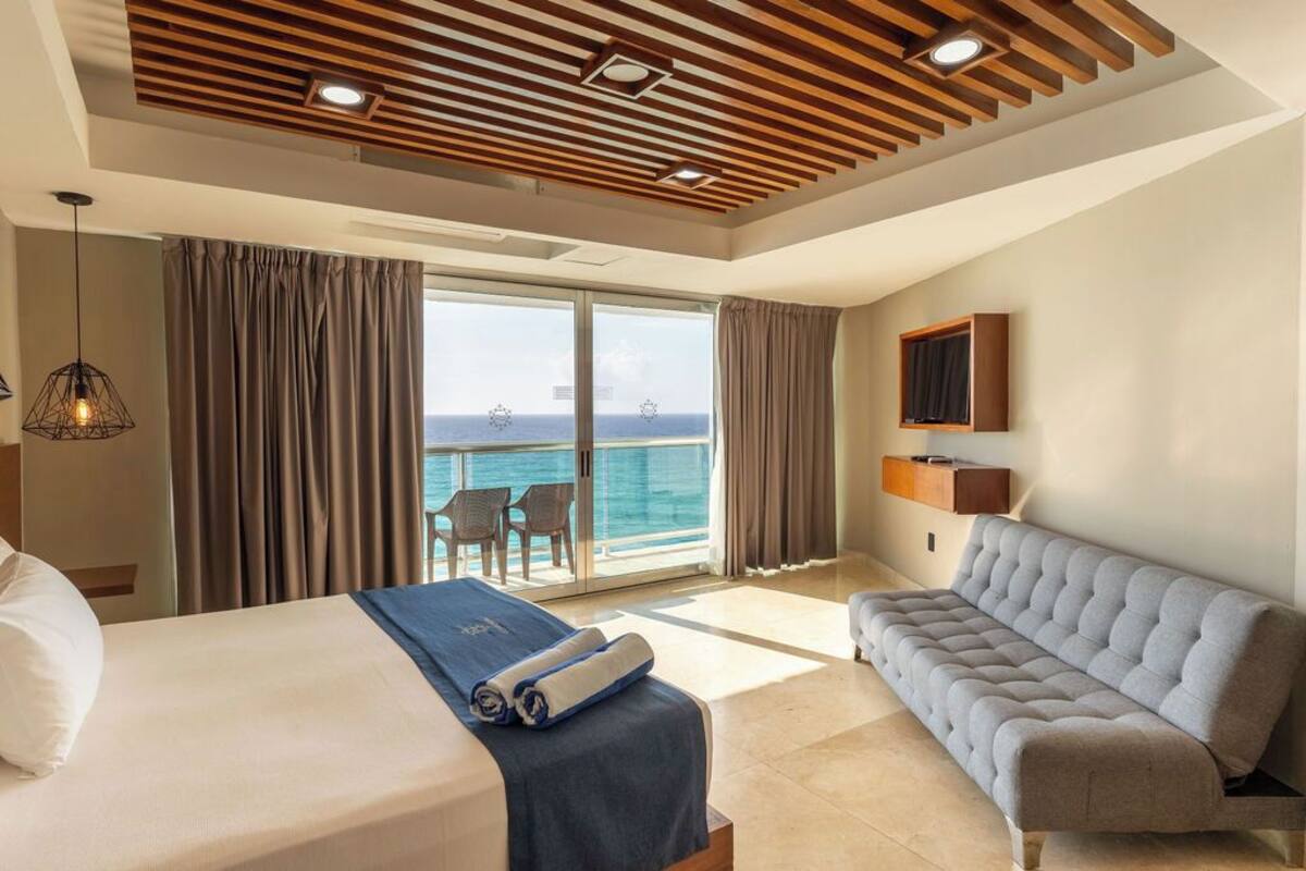 Ein Hotelzimmer mit Bett, einer Couch, einem Fernseher und einem Balkon mit Meerblick.