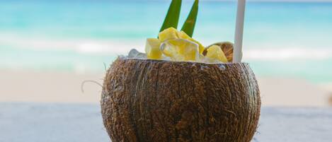 Bebida de coco con pajita y lima en una playa, con el océano al fondo.