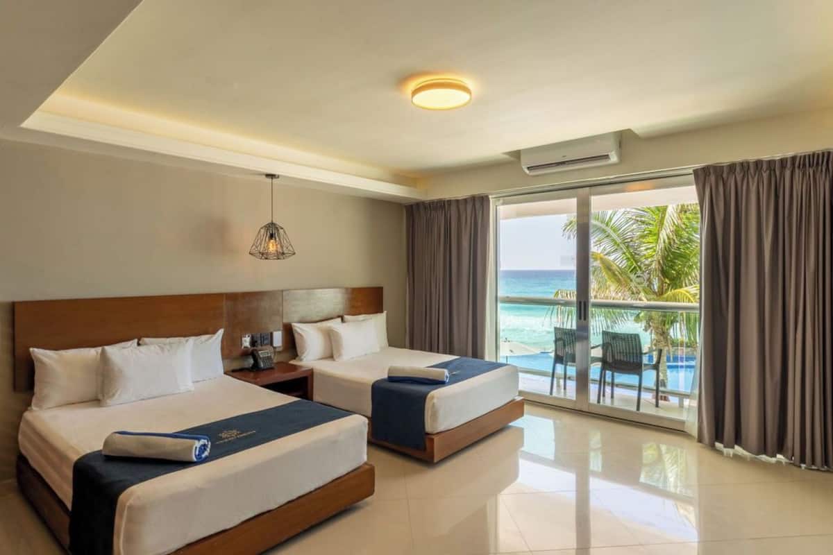 Ein Hotelzimmer mit zwei Betten, einem Nachttisch, einer Lampe und Blick aufs Meer.