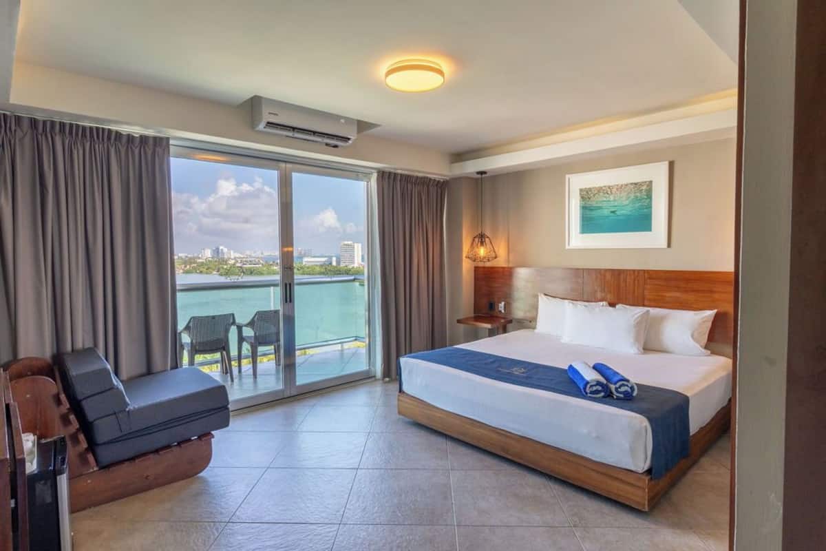 Ein Hotelzimmer mit Bett, Sitzgelegenheit, Blick auf das Wasser und die Stadtlandschaft.