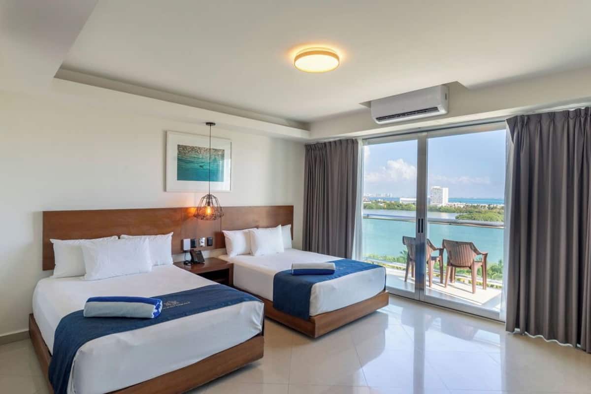 Ein Hotelzimmer mit zwei Betten, einem Nachttisch, einer Lampe, einem Gemälde und Blick auf das Meer.